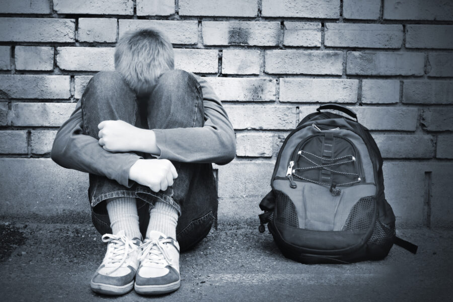 Homeless youth sitting on curb with backpack, at risk of exploitation