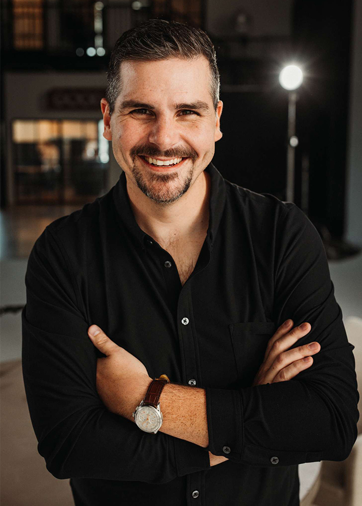 Photo of Clay Vaughan in a studio wearing a black shirt, arms crossed.